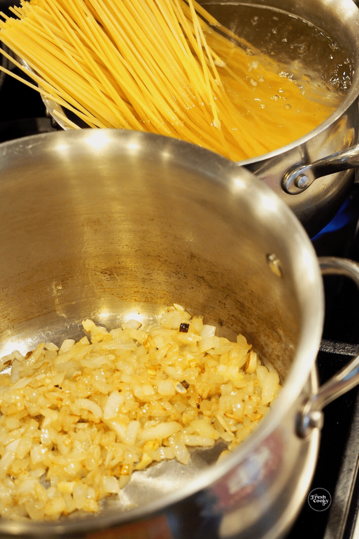 Browning onions and garlic with spaghetti cooking behind.