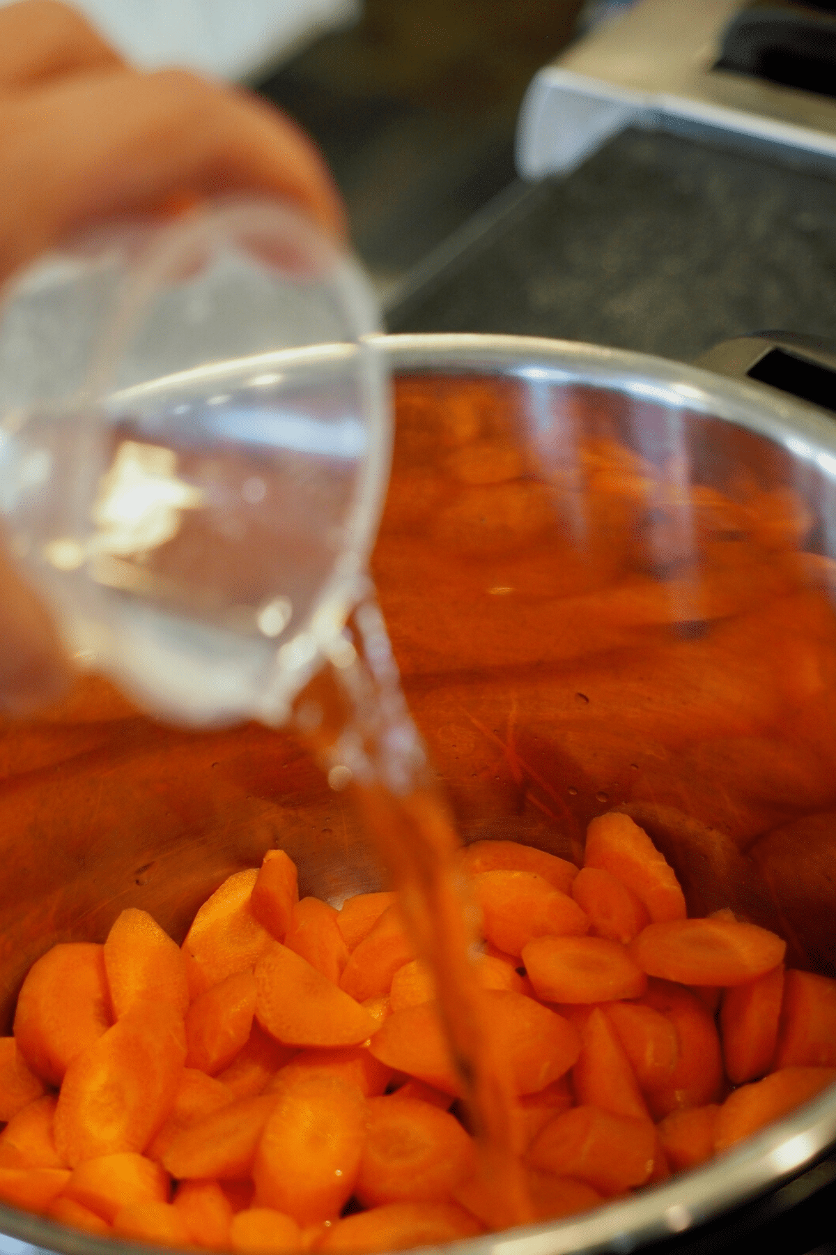 Pouring in water into instant pot on top of carrots. 