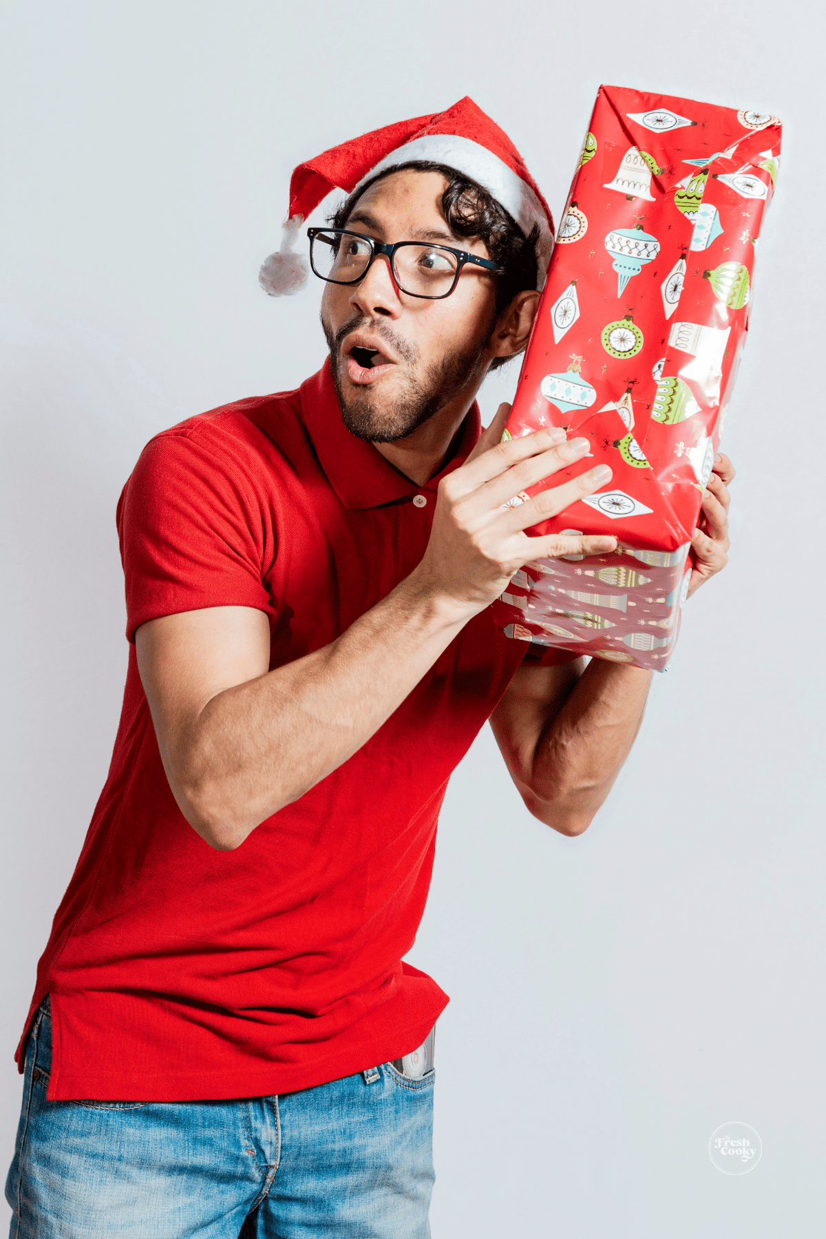 College guy holding a Christmas package up with a surprised look on his face.