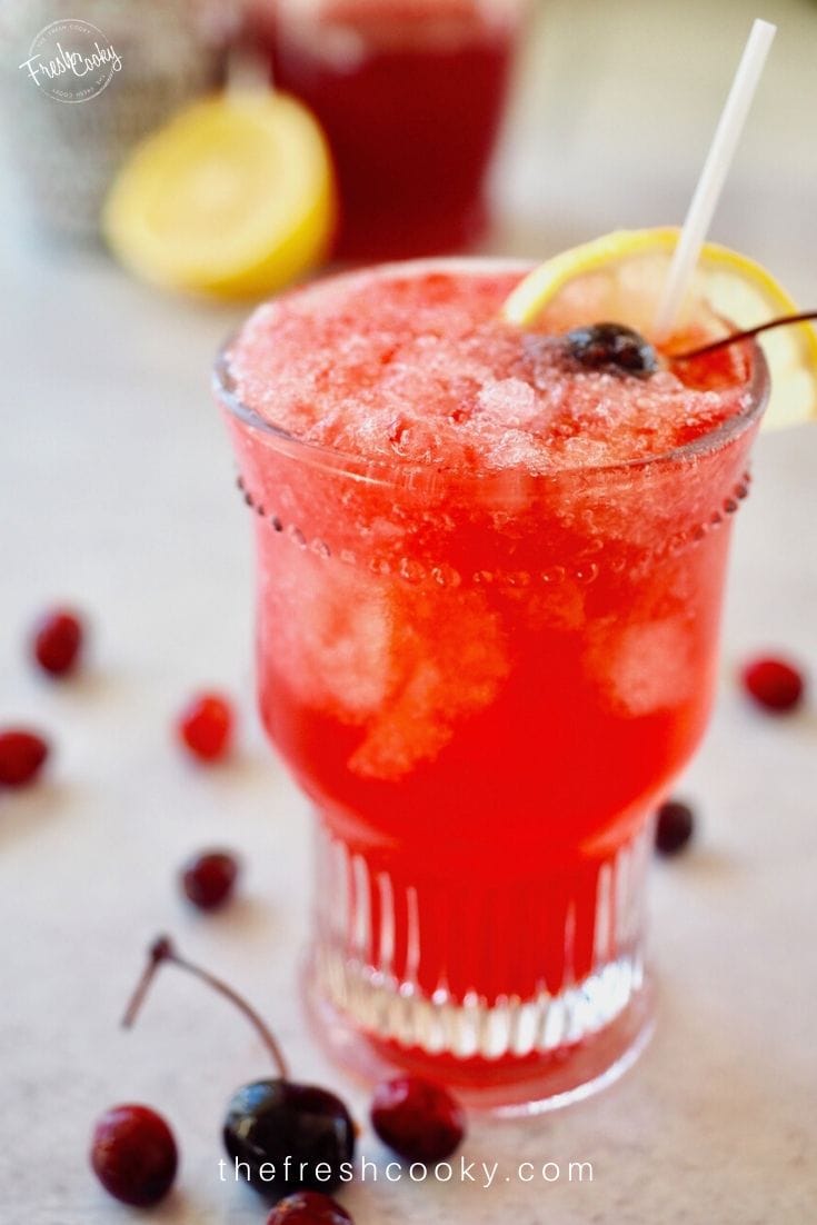 Pretty glass filled with bright red Cranberry Spritzer with cherries.