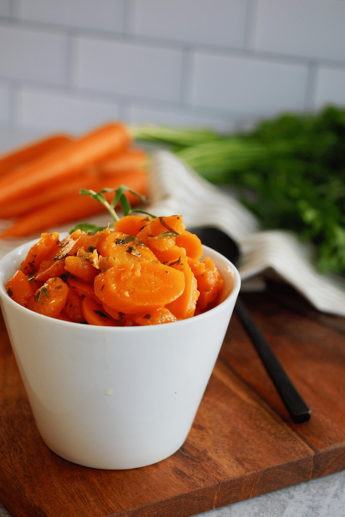 Tender Instant Pot carrots in bowl on board with fresh carrots with tops in background. 
