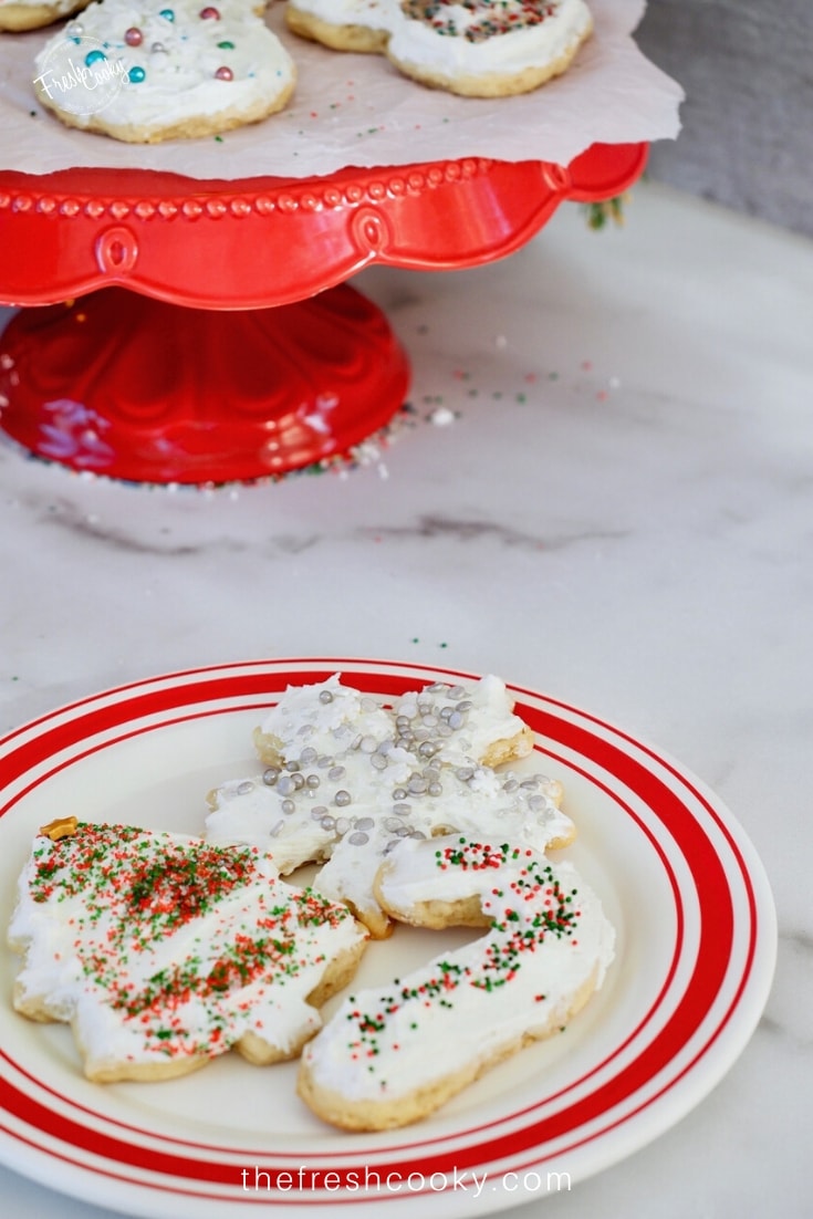 Red rimmed plate with three cutout Christmas cookies, frosted and covered in sprinkles. 