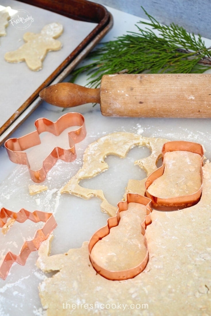 Cut out sugar cookie dough with oats, copper Christmas cookie cutters on marble.
