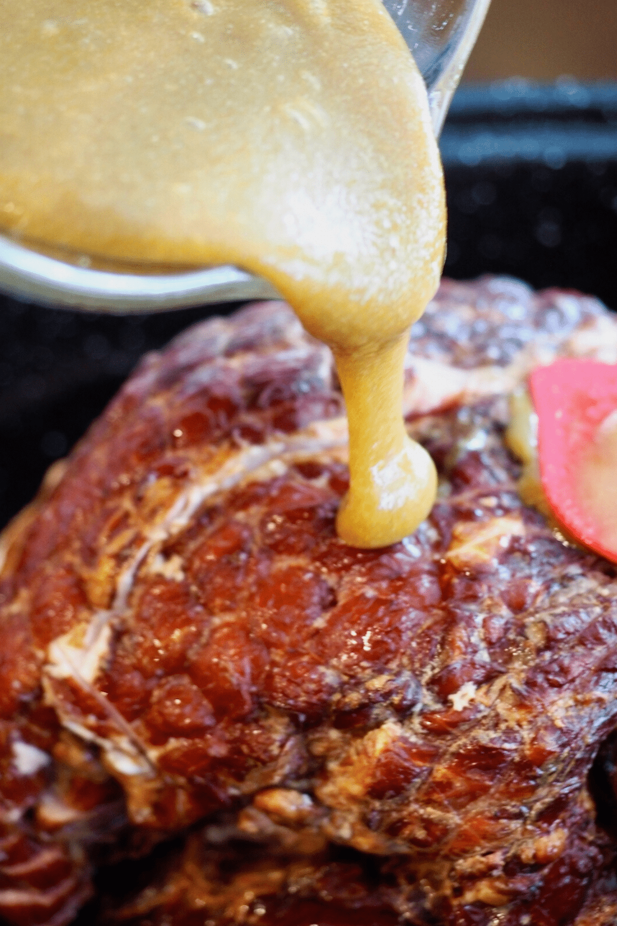Pouring brown sugar dijon glaze over top of ham. 