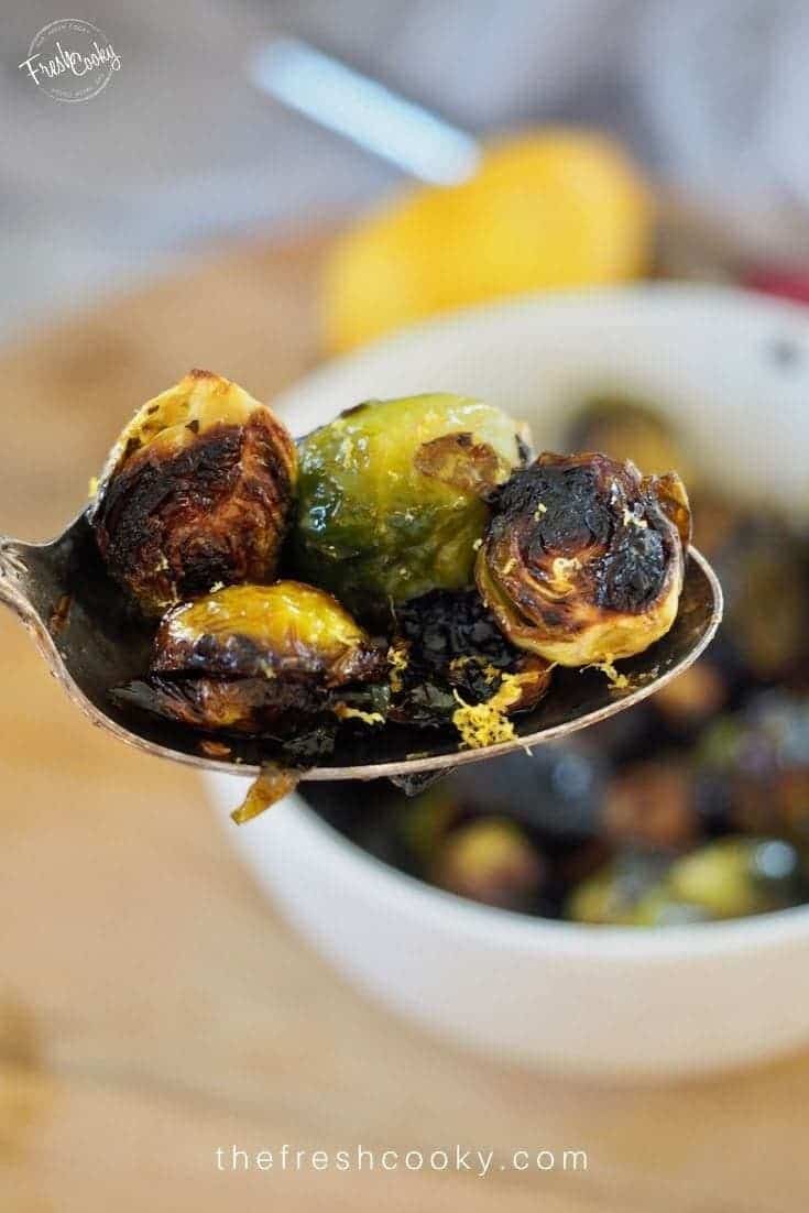 Spoonful of crispy roasted brussels sprouts with lemon in background and lemon zest on brussels. 