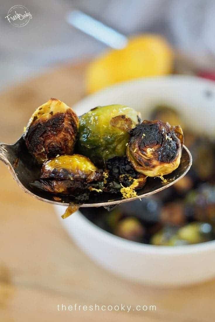 Spoonful of crispy brussels with lemon zest, with white bowl full of brussels in background.