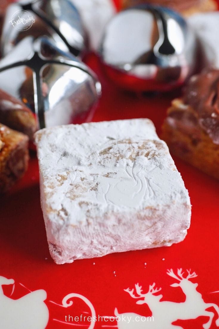 Close up image of a powdered sugar graham bite with silver jingle bells in background on red, Christmas plate. 
