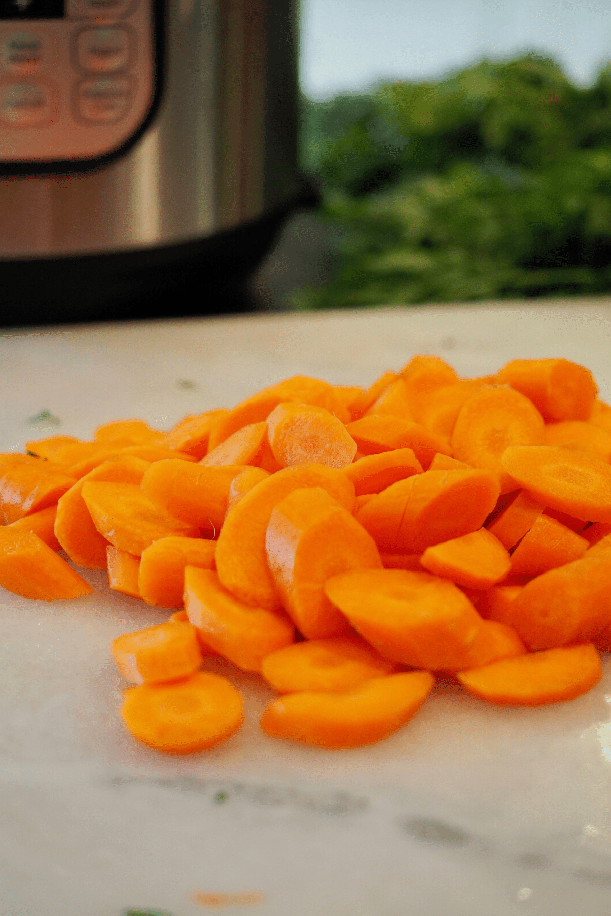 Sliced carrots on marble with instant pot in background. 