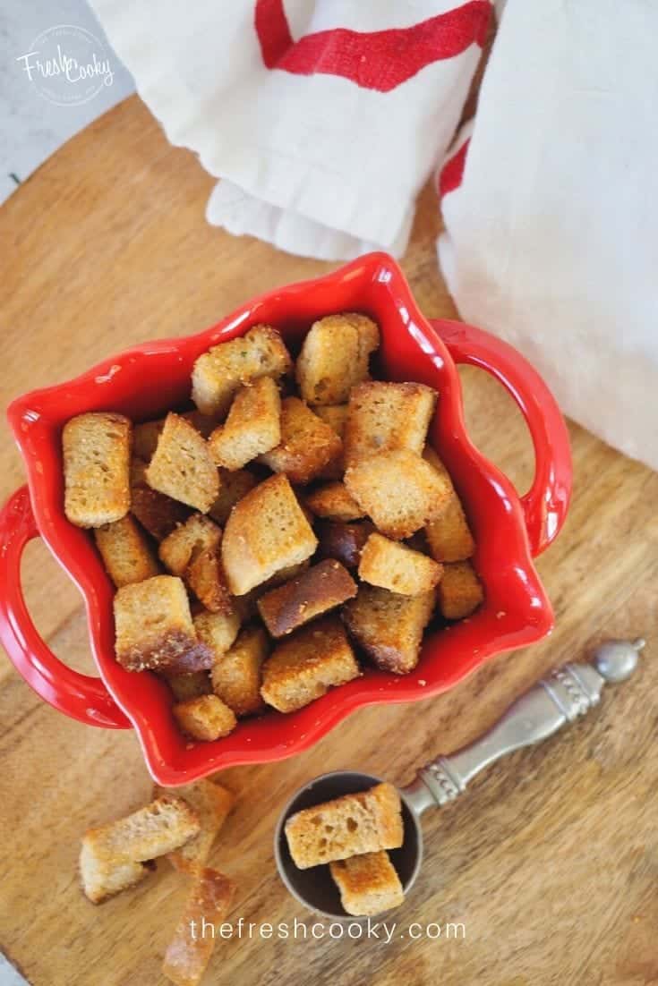 To down shot of crispy buttery croutons in red bowl with some sprinkled outside of the bowl. 