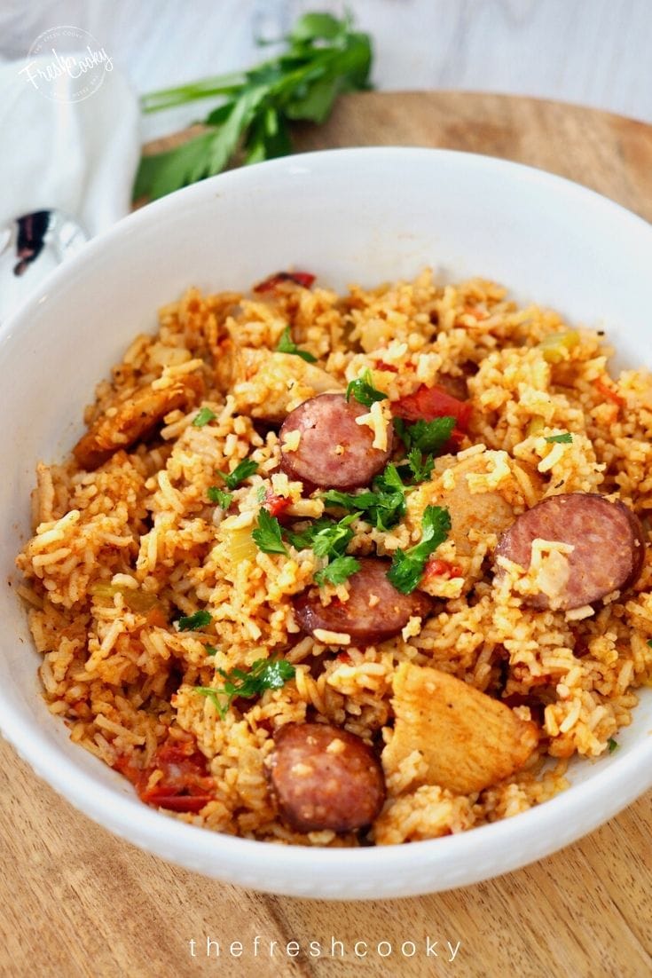 large white bowl filled with chicken and sausage jambalaya on wooden charger with cilantro in background