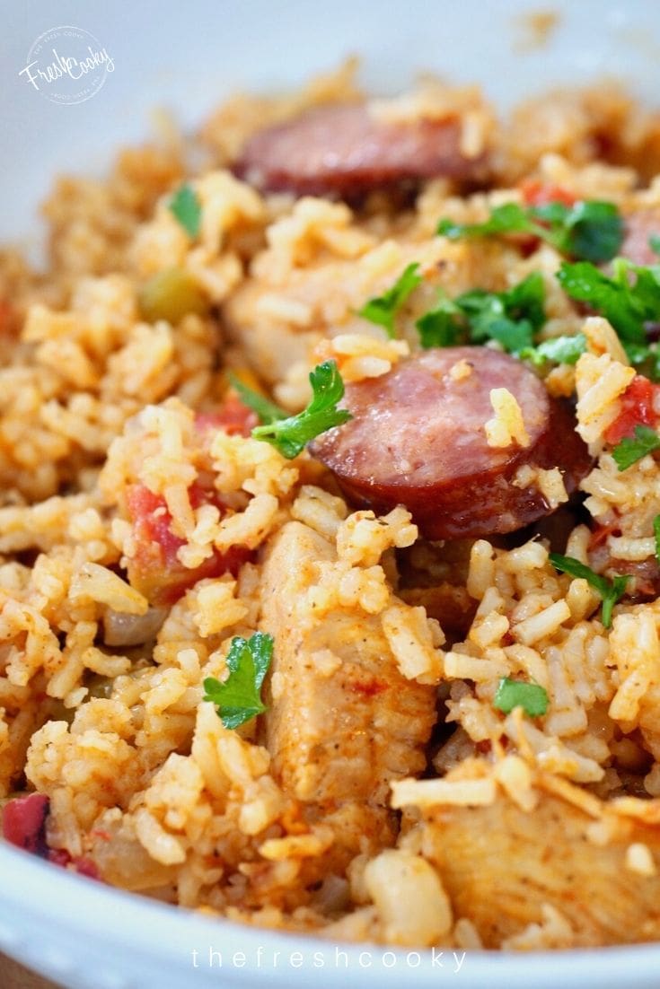 Close up shot of chicken and sausage jambalaya, with sausage slice and dirty looking rice from teh tomatoes, and a sprinkling of bright green parsley!