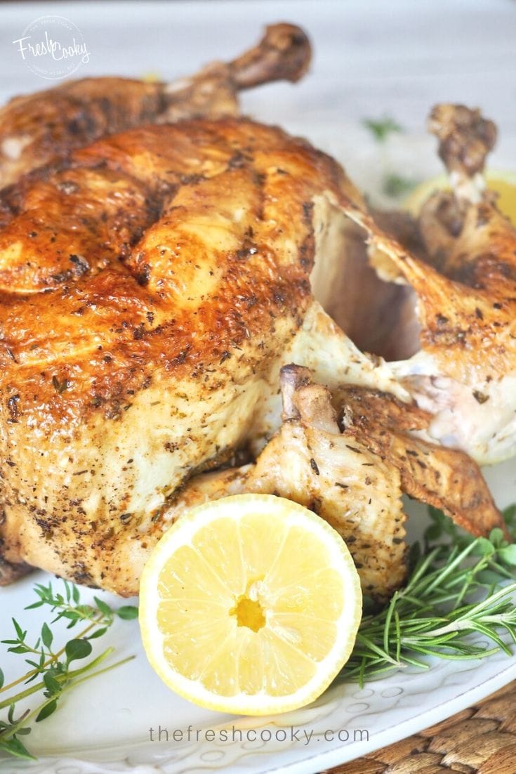 instant pot rotisserie chicken on a tray with lemon and fresh herbs. whole chicken