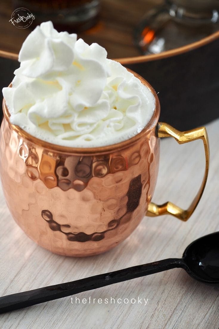 Copper mug filled with creamy hot buttered rum topped with whipped cream. 