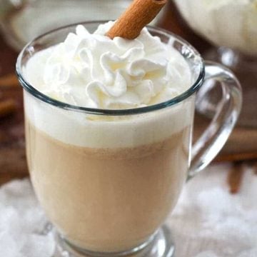 Mug filled with creamy hot buttered rum topped with whipped cream and a cinnamon stick.