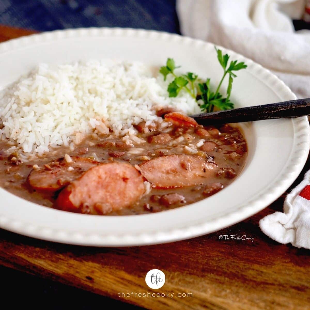 Square image for Slow Cooker Red Beans and Rice with bowl of red beans and white rice sitting on a cutting board with a rustic spoon.