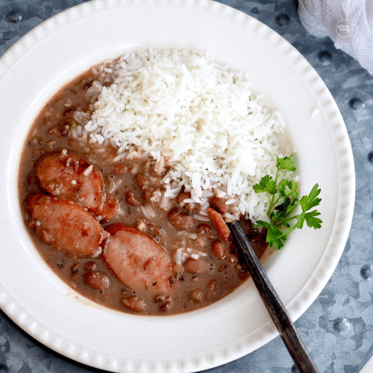 Bowl filled with slow cooker red beans and rice with andouille sausage, ham and smoked chicken.