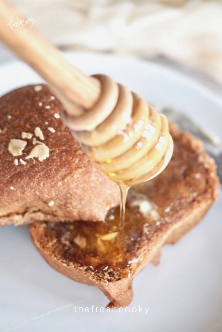 Close up image of a sweet molasses brown bread roll with butter and honey dripping onto the roll