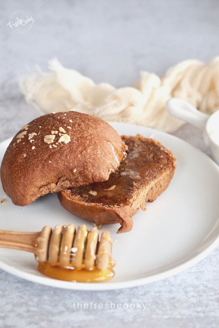 image of roll sliced in half on a white plate with a honey stick oozing onto the plate. 