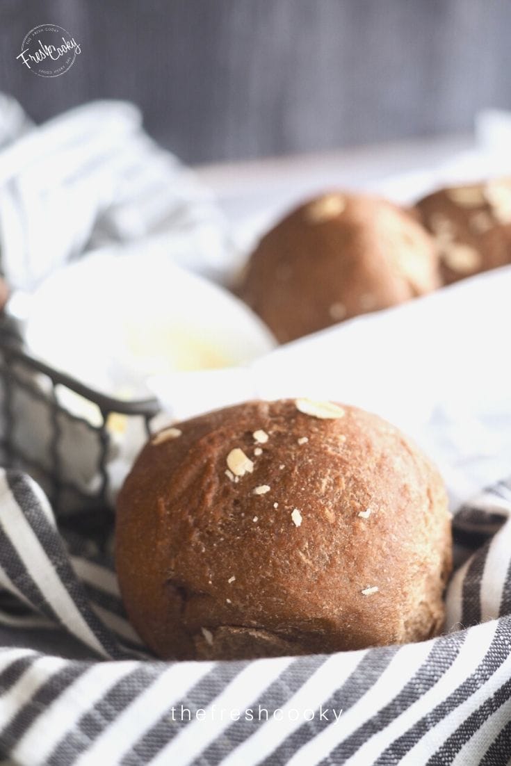 Basket lined with striped napkin with a brown roll sitting inside. 