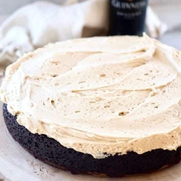 high altitude Chocolate Guinness Cake with Irish Buttercream frosting on a slice of wood with a bottle of Guinness in the background