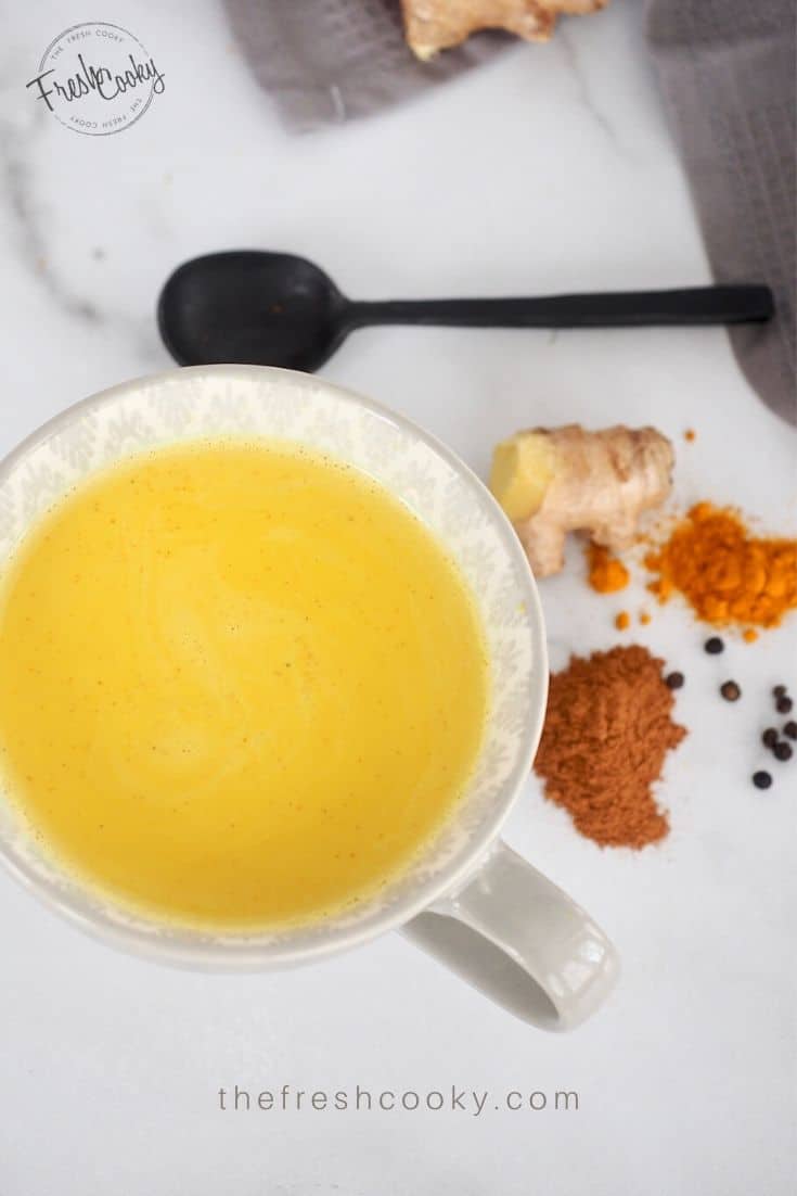 Top down shot of Golden Milk Turmeric Tea in grey mug with spices on counter. 