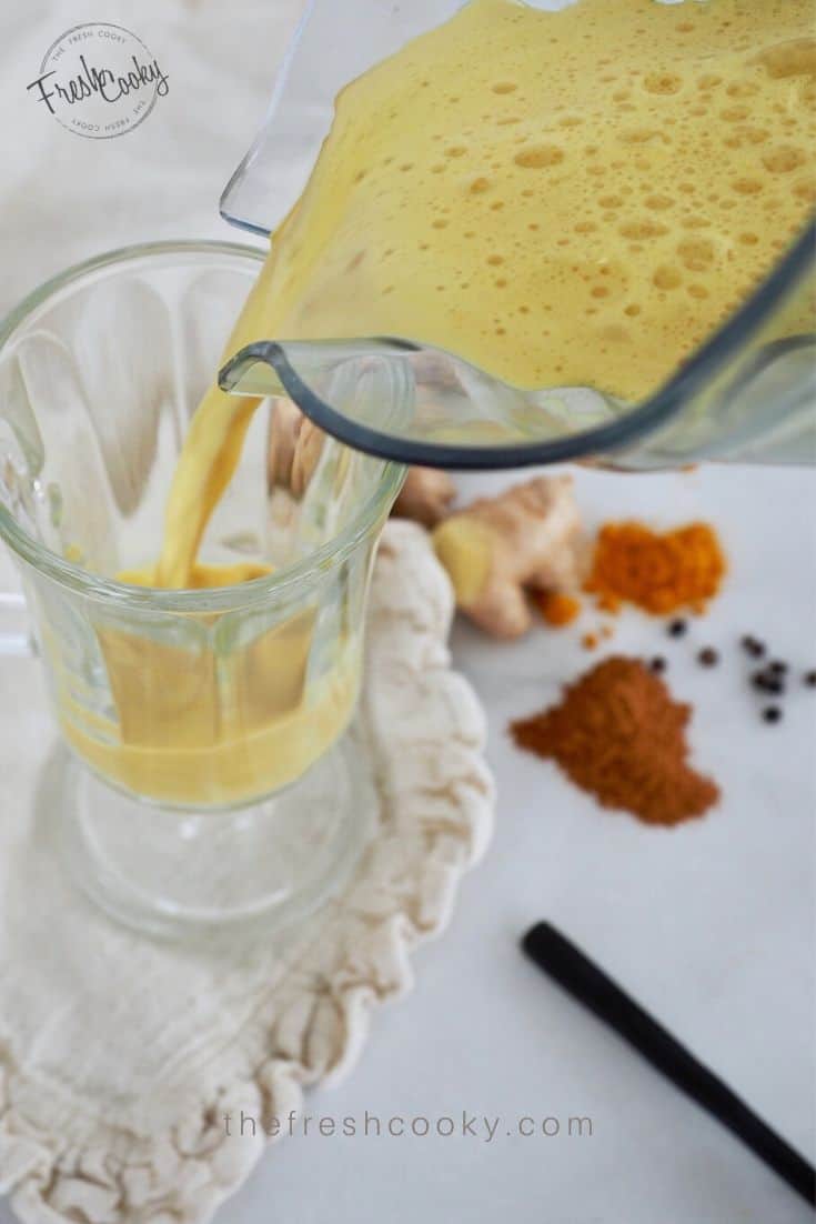 Glass mug with golden milk tea in it with a spoon and spices on the counter. 