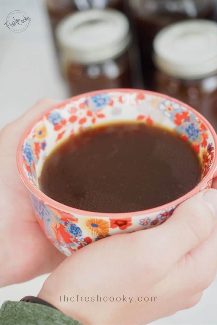 Hands holding beef broth in a mug.