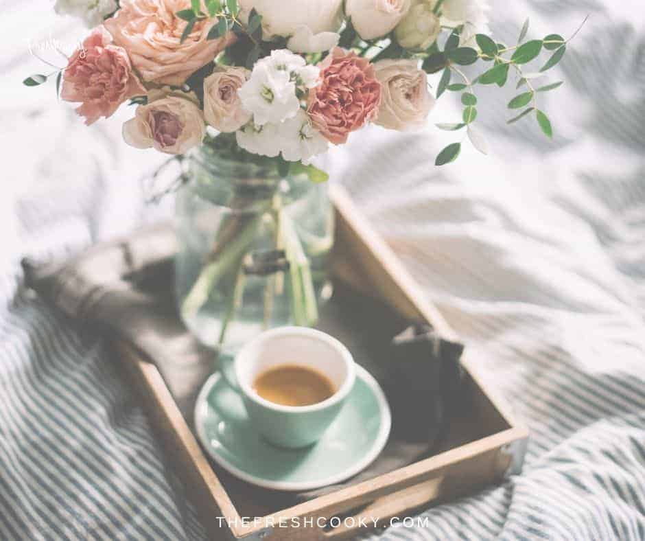 Mother's day image with a try with a cup of coffee and a vase of flowers on a comforter on a bed.