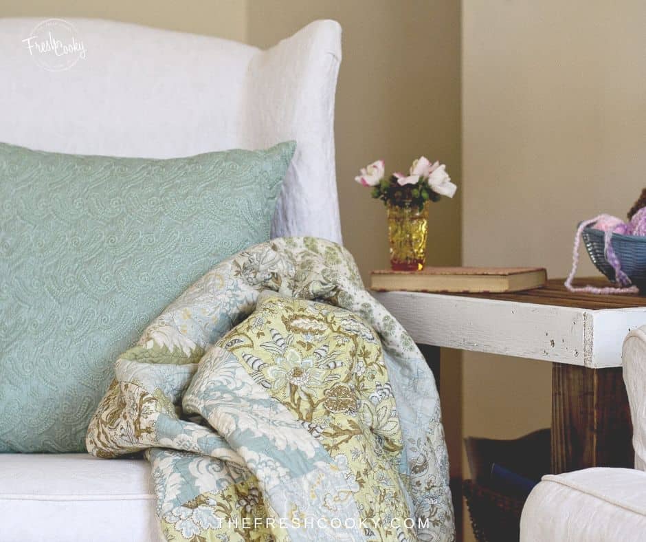 Pretty comfy chair in the corner with a pastel quilt ready for snuggling in to. 