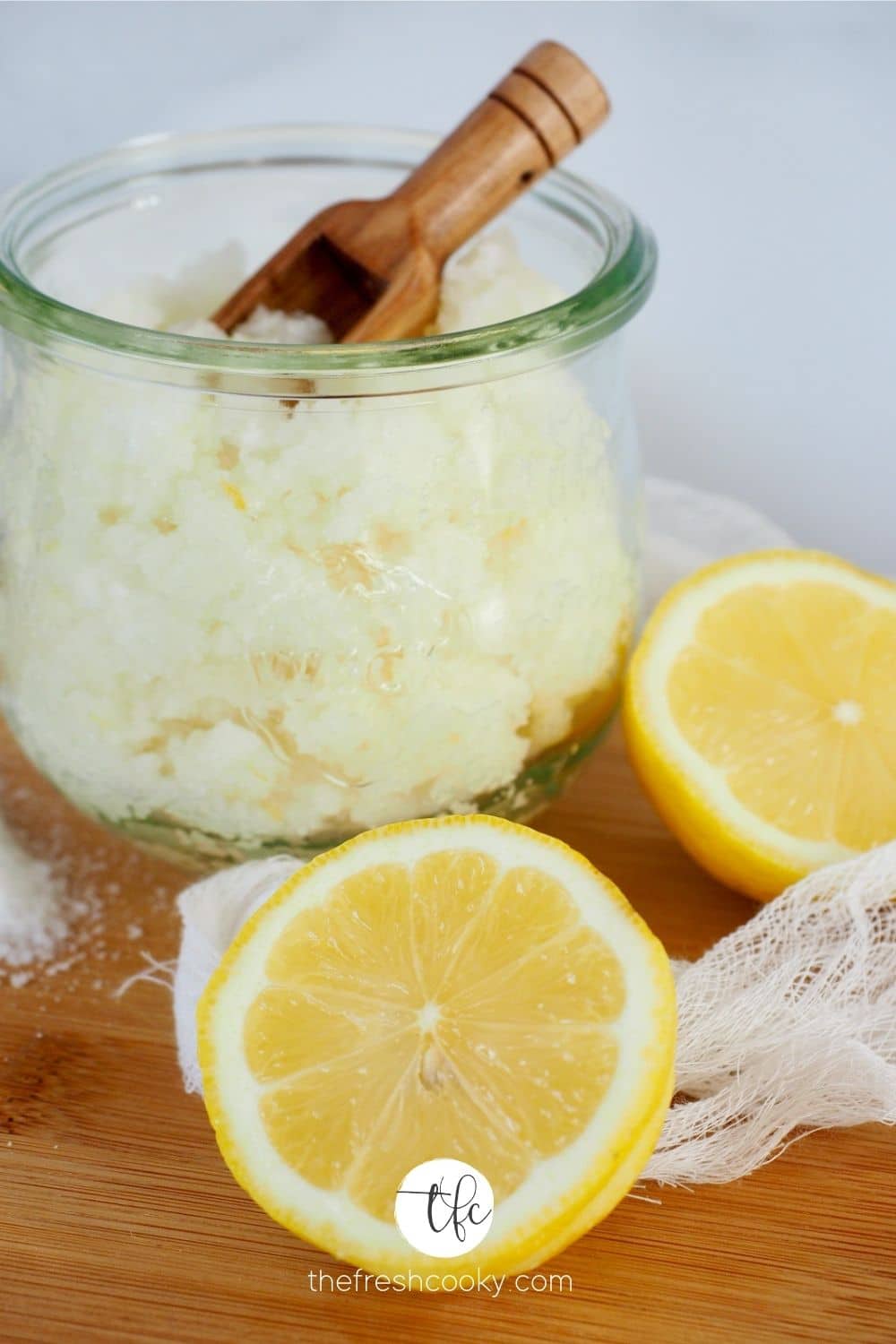 Open glass jar with wooden scoop inside of lemon peppermint antibacterial hand scrub.