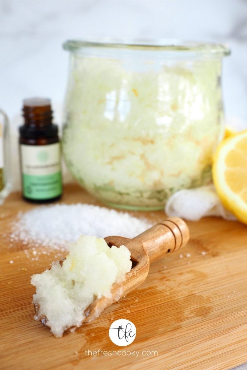 Lemon Peppermint Antibacterial Hand Scrub on cutting board with essential oils and scooper filled with salt scrub.