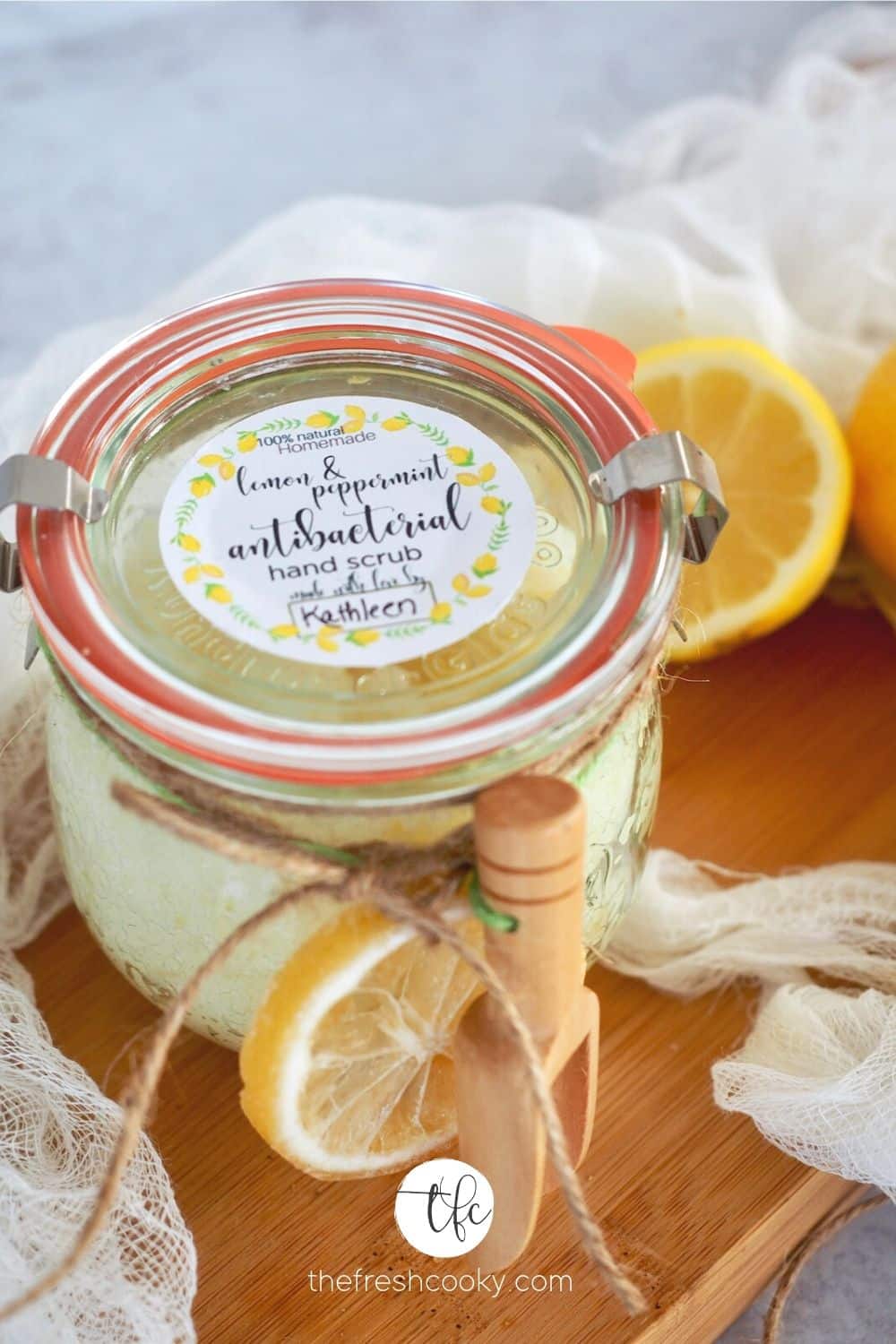 Top down shot of jar of lemon peppermint antibacterial hand scrub with free label, tied with dried lemon and a wooden scoop.