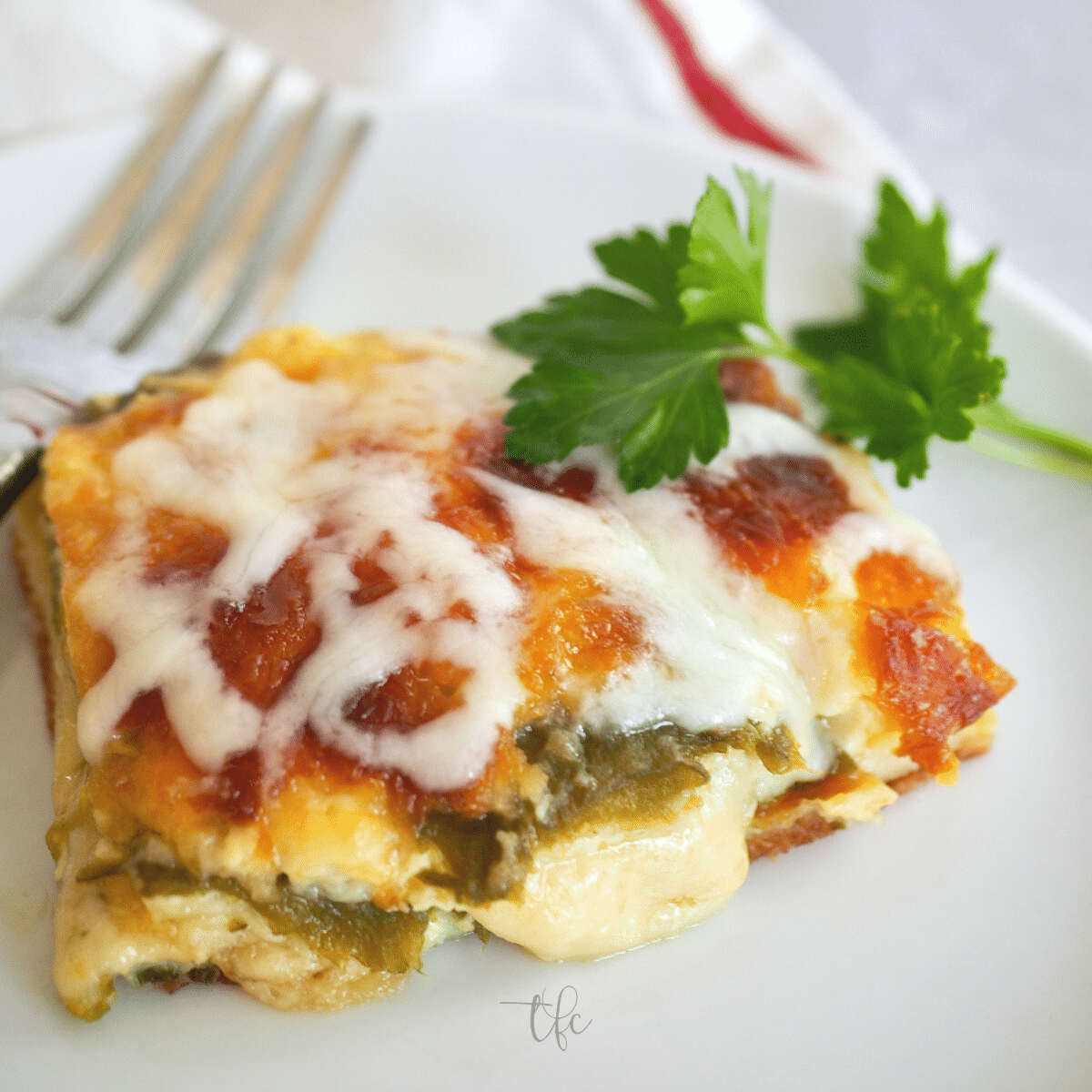 Square of chile relleno casserole on a plate with a fork and cheese oozing from chile.