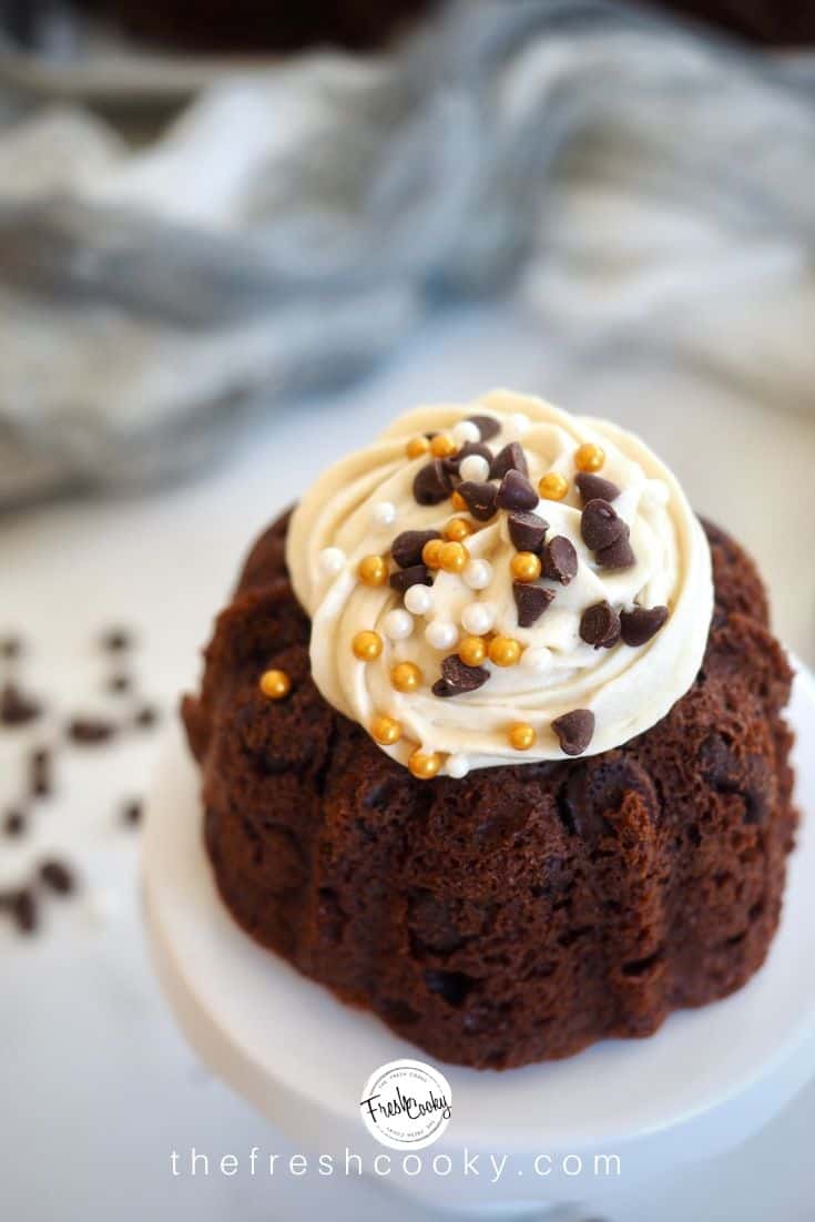 Close up of a chocolate chocolate chip mini bundt cake topped with a creamy swirl of brown sugar cream cheese frosting, sprinkled with pearl and gold sprinkles and mini chocolate chips. via thefreshcooky.com 