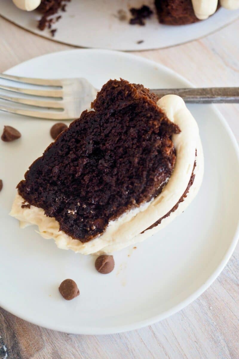 Slice of rich chocolate cake on a white plate with a fork beside. 