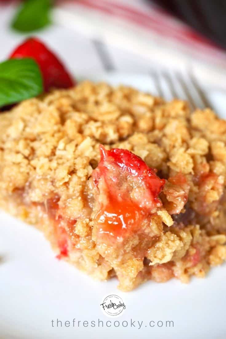 Square of strawberry rhubarb crumb bar on plate with fork and strawberries. 