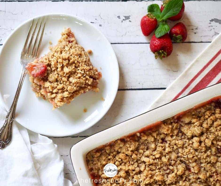 Image of slice of strawberry rhubarb crisp bar on plate with crisp nearby. 