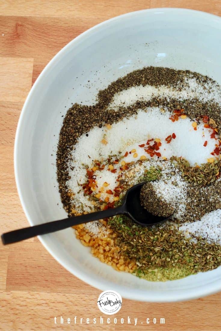 white bowl of swirled/stirred spices for dry rub with black spoon.