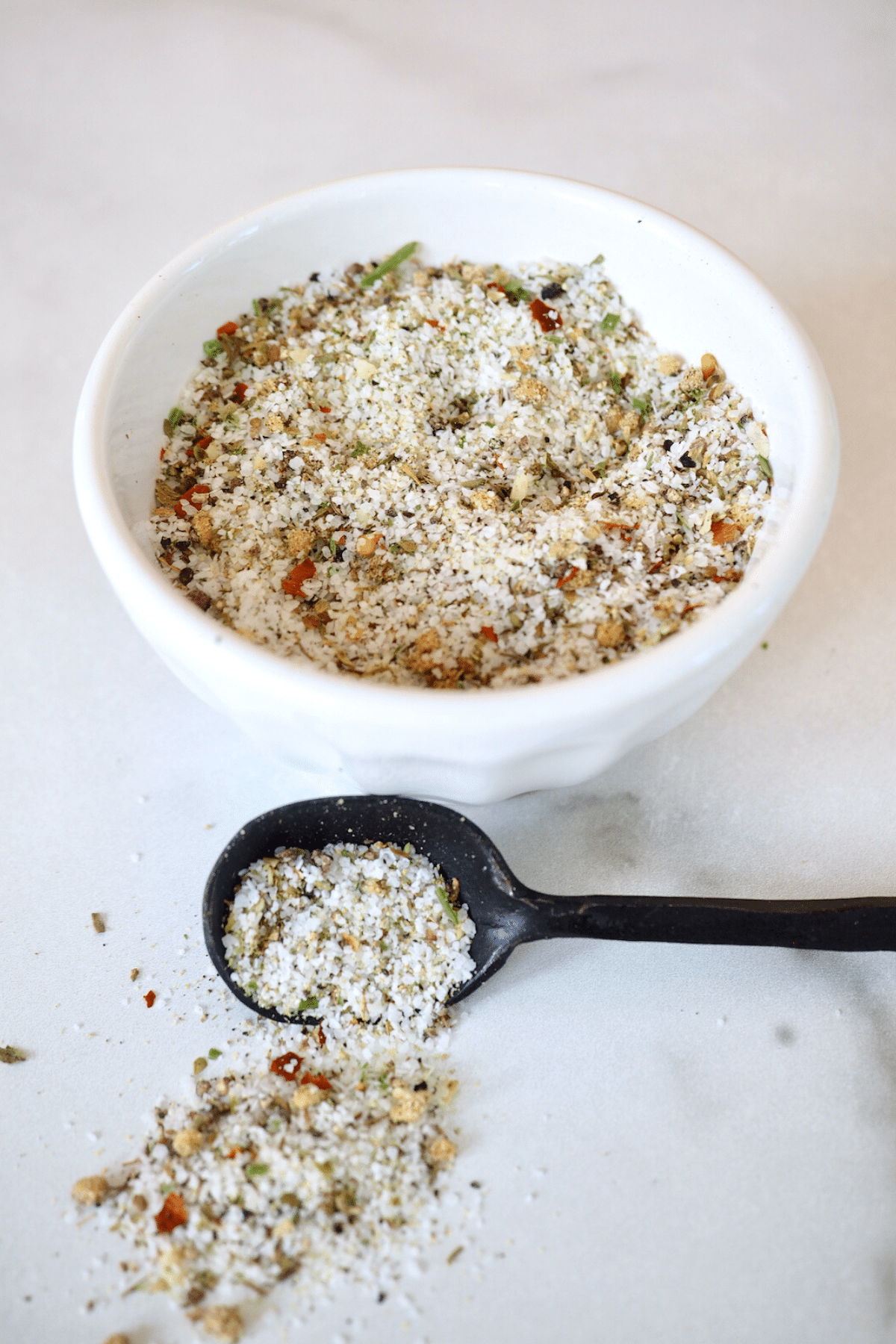 Bowl filled with Carrabba's grill seasoning with black spoon with spilled seasoning on table.