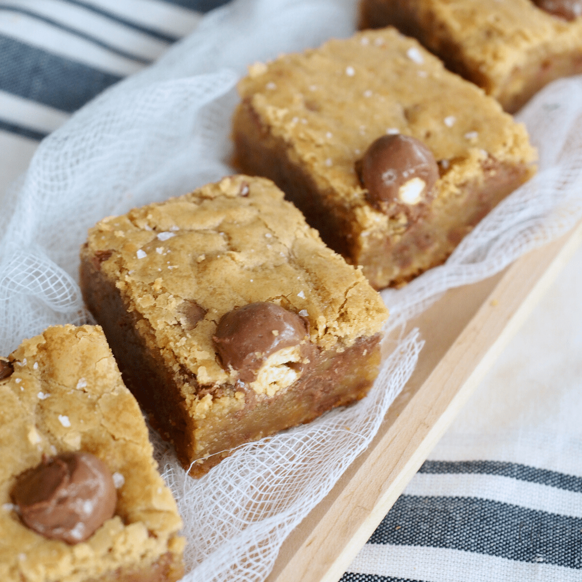 Easy Chewy Blondies cut on a wooden tray with whoppers malted milk balls in them. 