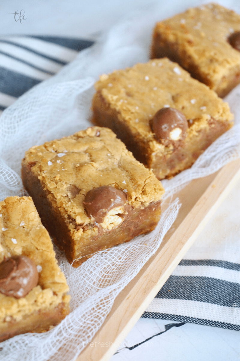 Best Chewy Blondies on a wooden tray with malted milk balls in them.
