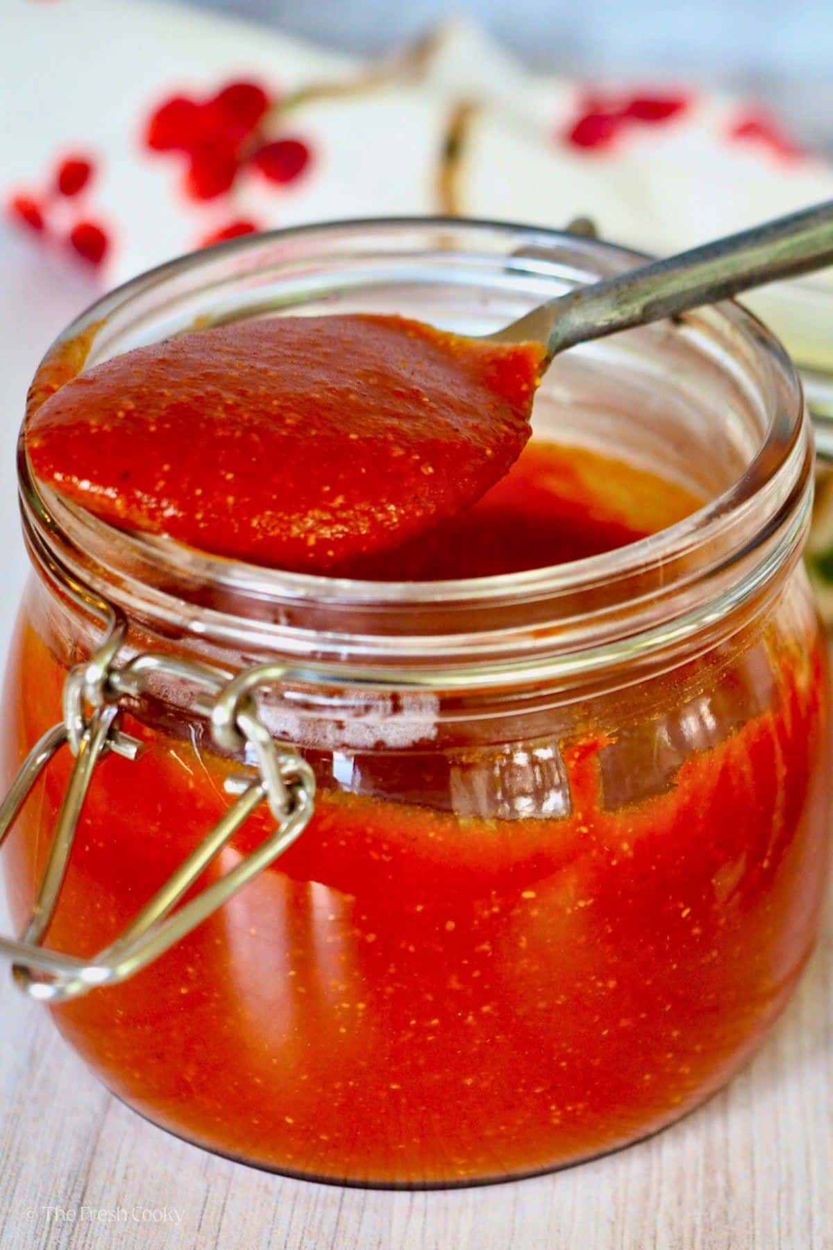 Spoon full of barbecue sauce resting on the rim of a jar filled with sauce. 