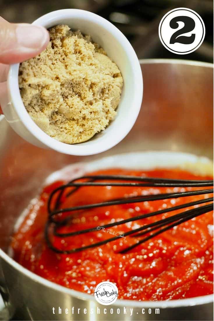 small white bowl with brown sugar over mixture of ketchup and butter with black whisk showing.