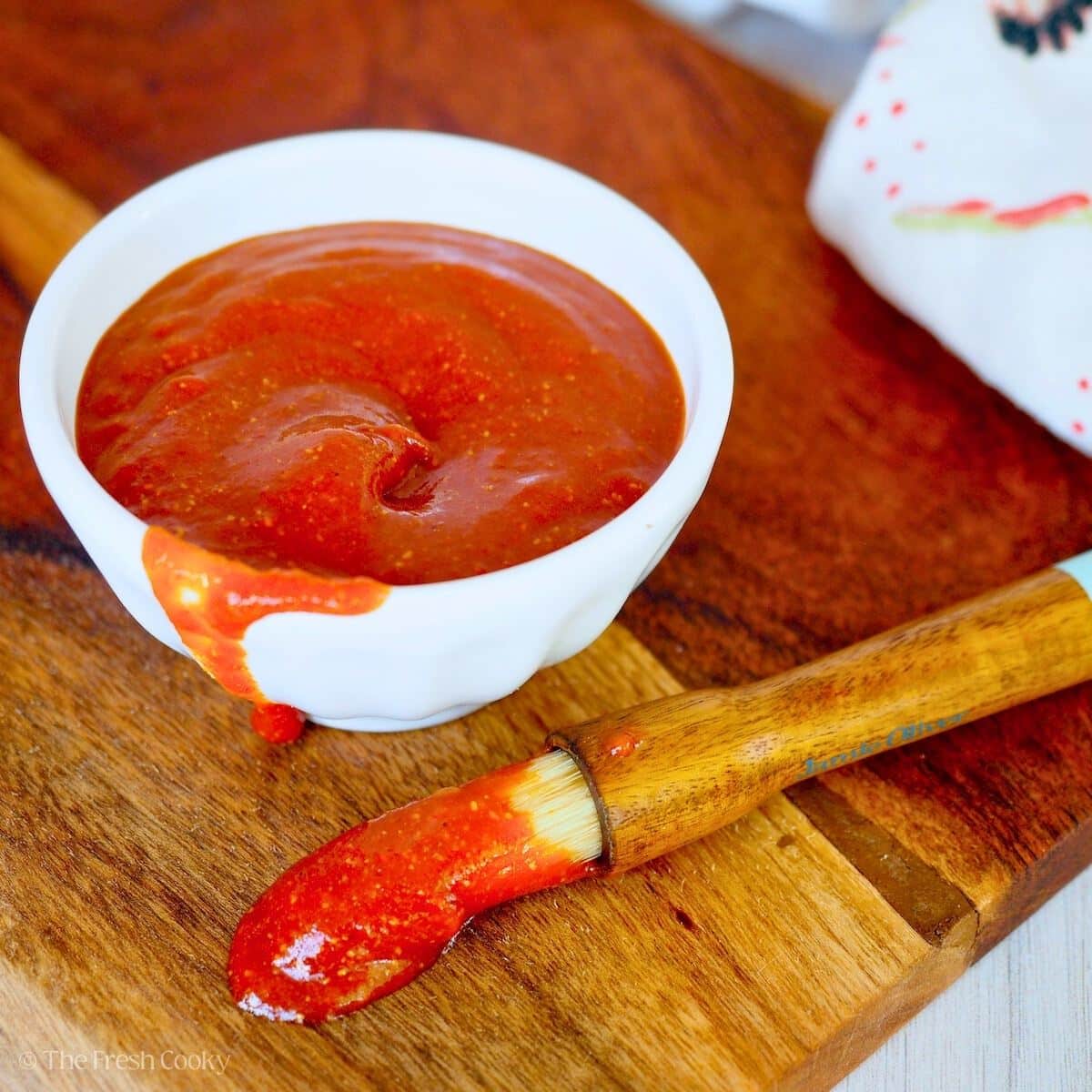 Homemade barbecue sauce in a cup with a basting brush.