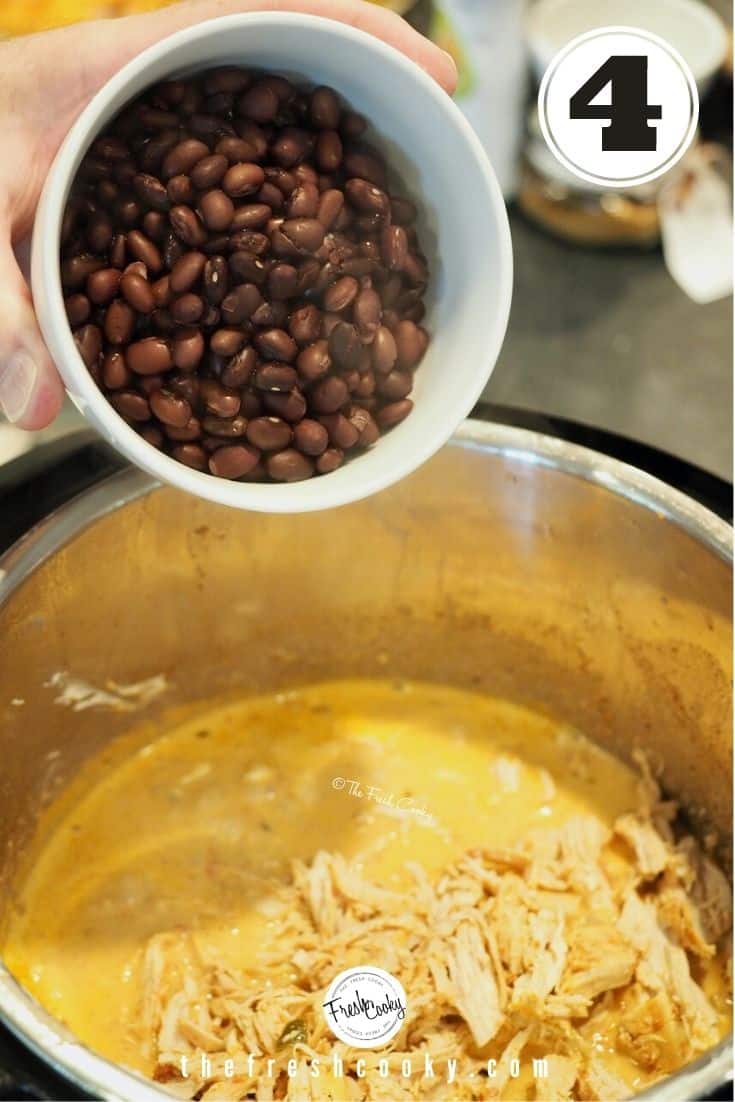 A white bowl with black beans being poured into creamy crack chicken 