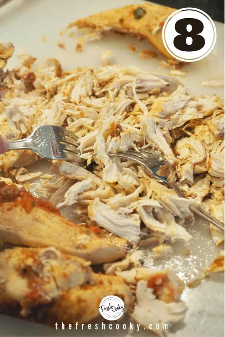 two forks with shredded chicken on a cutting board