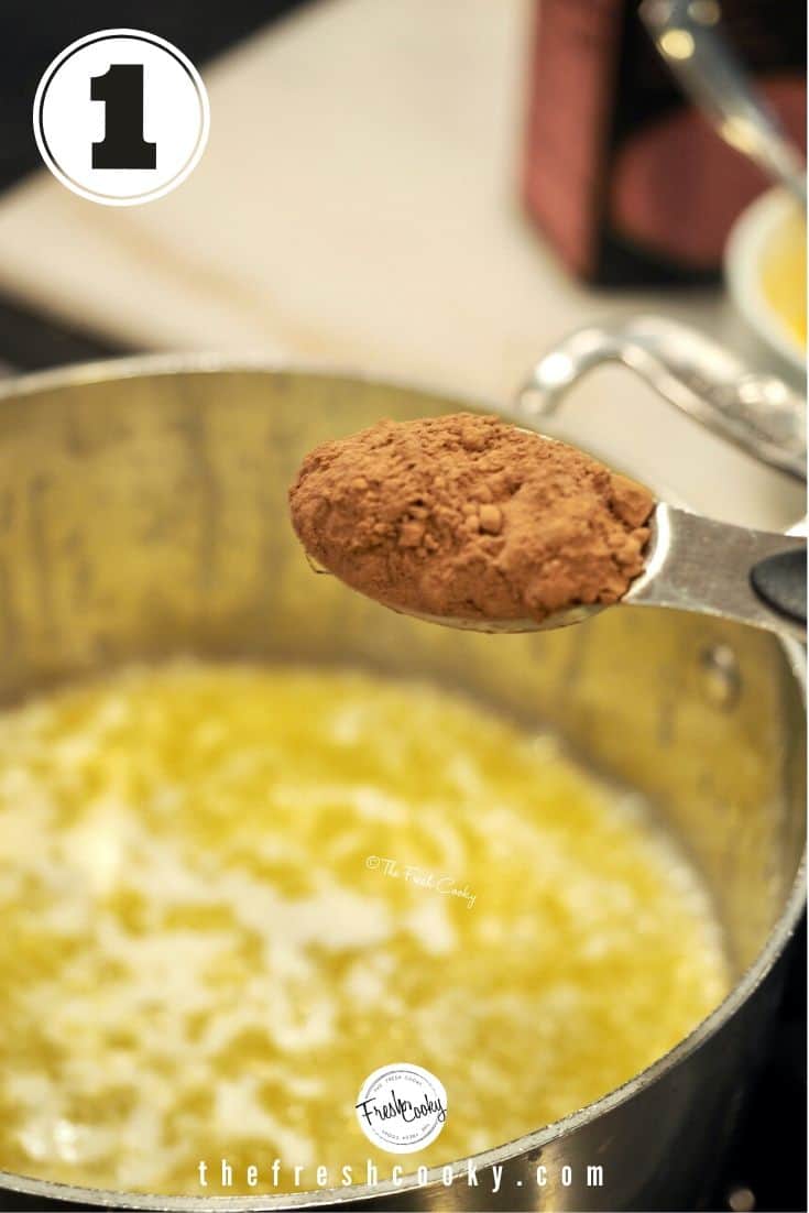 Tablespoon with rounded spoon of cocoa powder over saucepan of melted butter