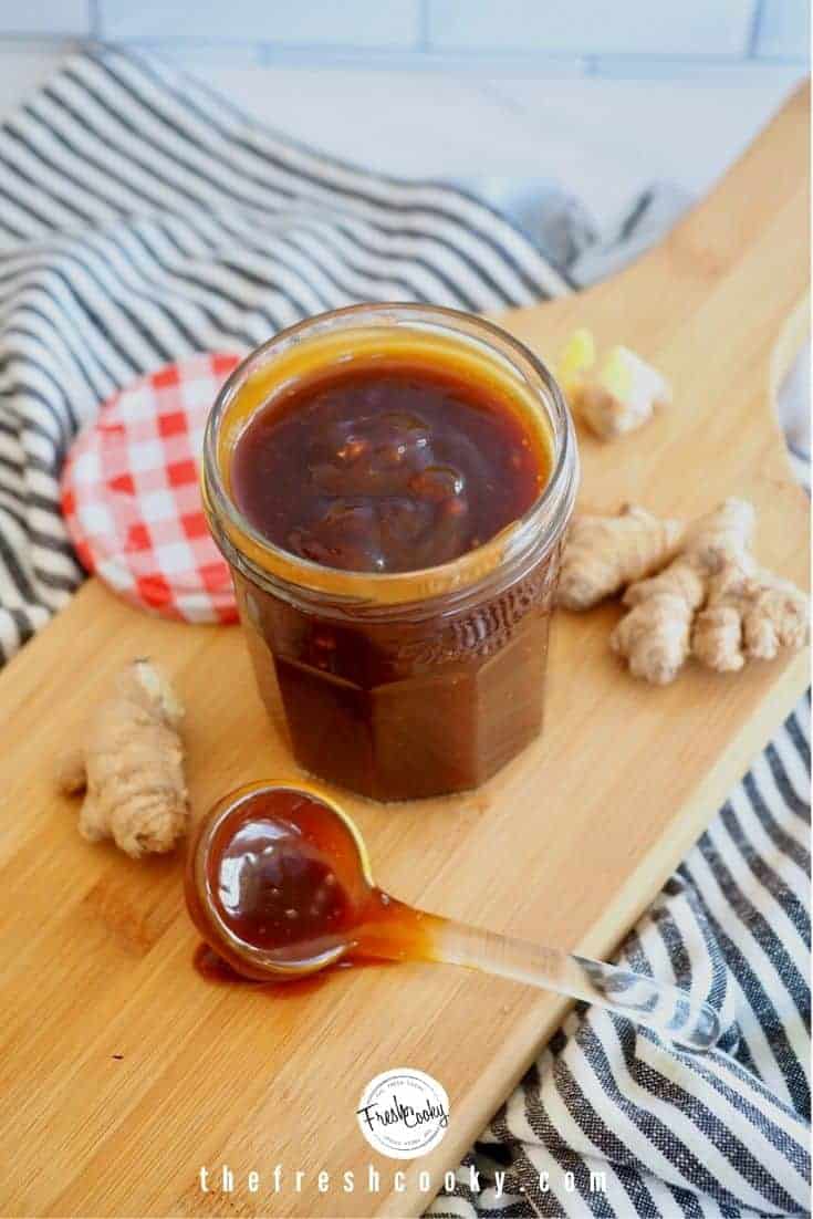 jar of teriyaki sauce on cutting board with glass ladle and ginger in background.