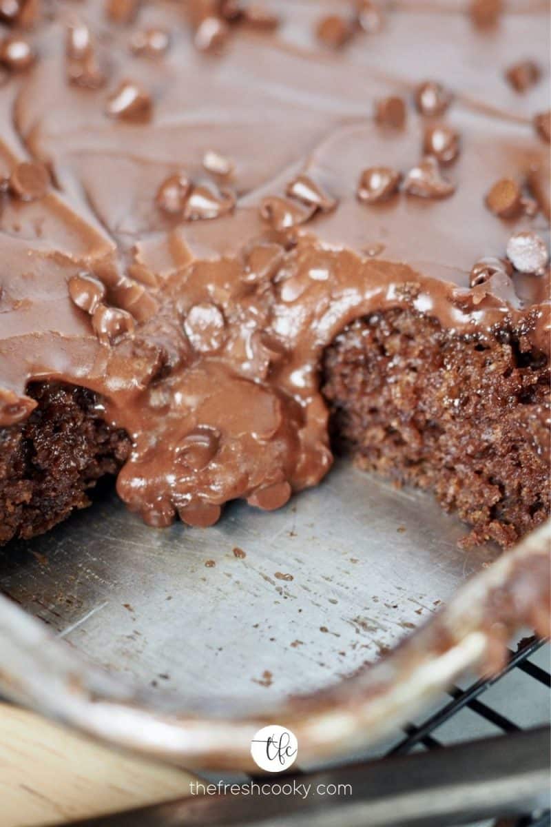 Shot of Texas Sheet Cake in pan with corner piece removed and fudgy frosting oozing onto the pan.