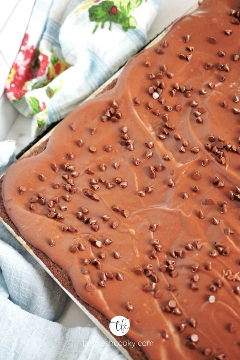 Top down shot of the corner of the best Texas Chocolate Sheet Cake with pretty summery tea towel by it's side.